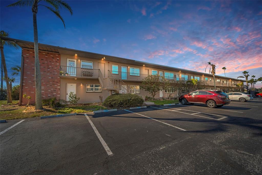 A two-story apartment building with a brick facade and parking lot at sunset — 2 CAUSEWAY BOULEVARD UNIT 208, DUNEDIN, FL