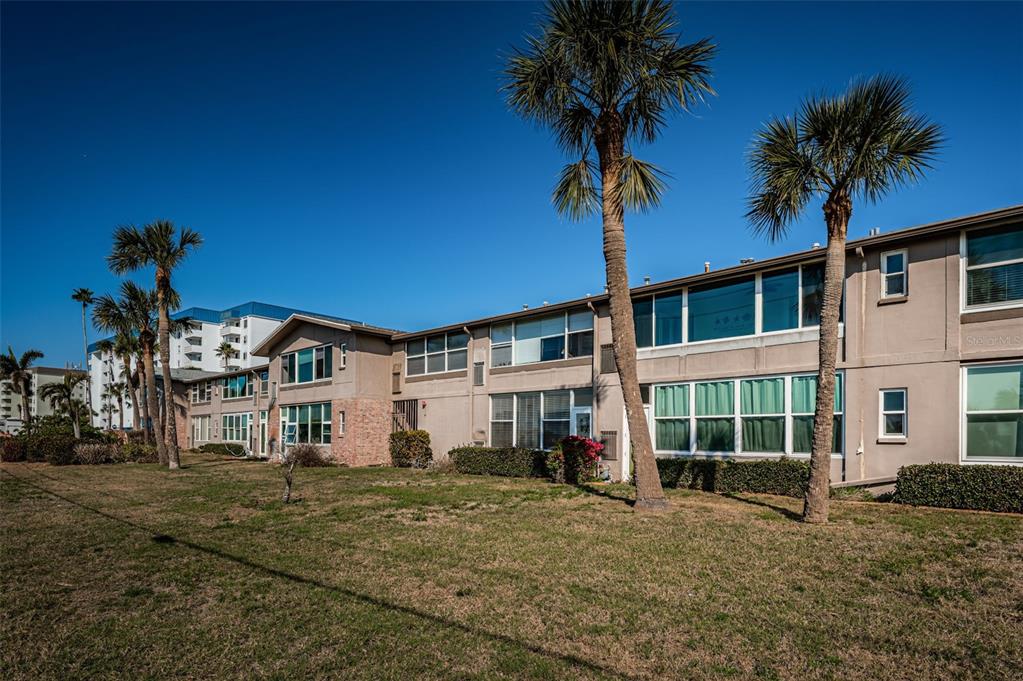 A multi-story apartment building with palm trees and a grassy lawn in the foreground — 2 CAUSEWAY BOULEVARD UNIT 208, DUNEDIN, FL