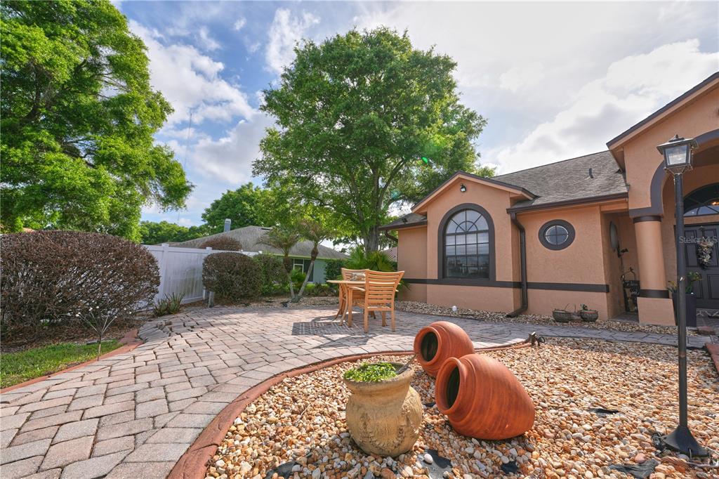 A paved patio with a wooden table and chairs sits beside a tan stucco house — 103 OLYMPUS DRIVE, OCOEE, FL