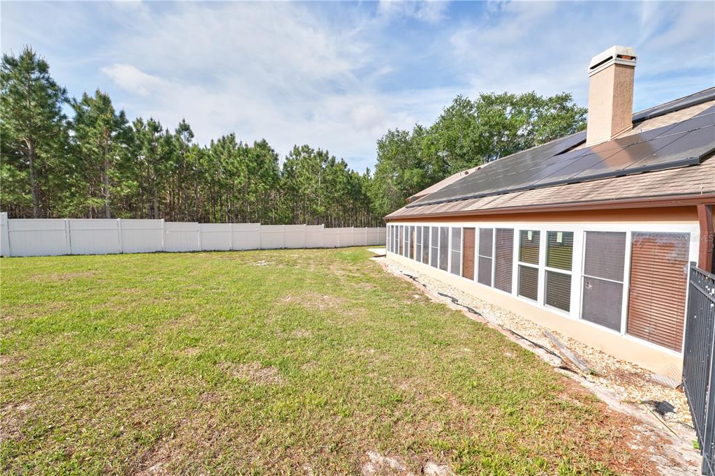 A backyard features a grassy lawn, a white vinyl fence, and a house with solar panels — 103 OLYMPUS DRIVE, OCOEE, FL