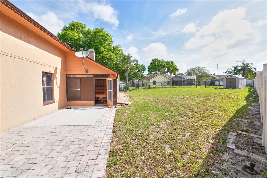 A paved patio sits beside a house with a screened porch and a large backyard — 103 OLYMPUS DRIVE, OCOEE, FL