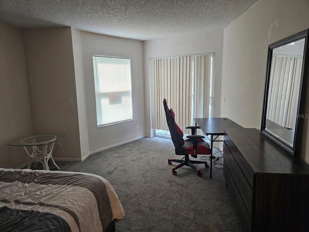 A bedroom with gray carpet, a desk, a gaming chair, and a sliding glass door — 2430 LEMON TREE LANE UNIT 2I, ORLANDO, FL