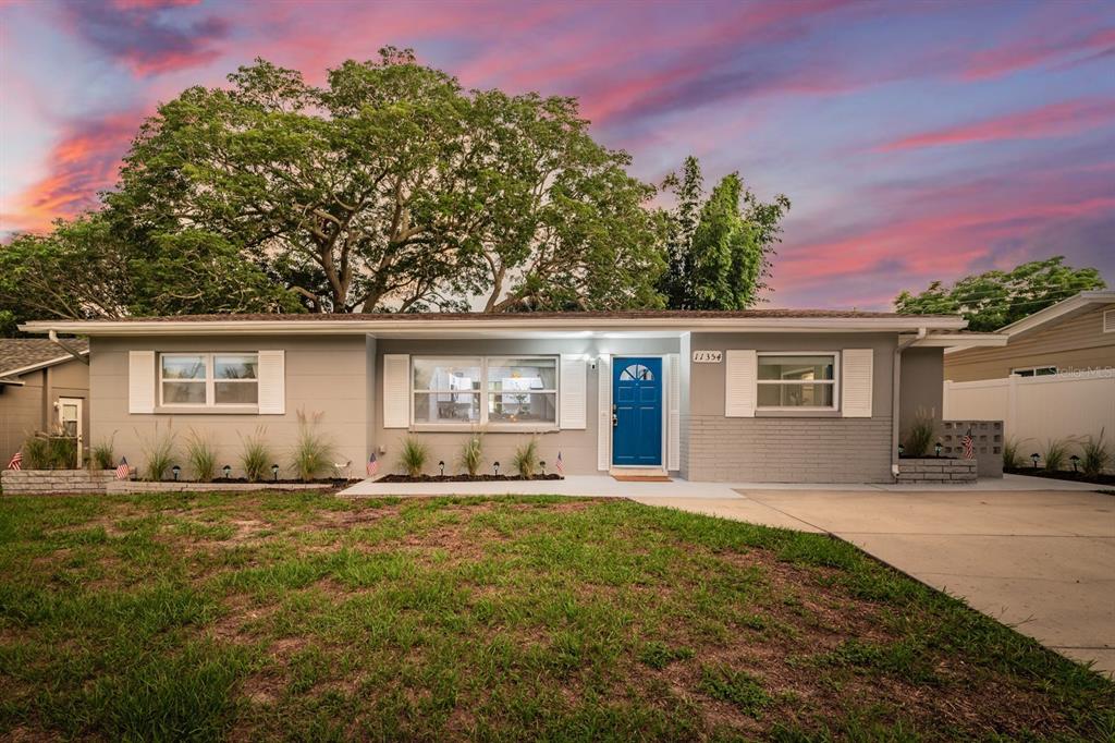 A single-story gray house with a blue front door and white shutters sits at dusk — 11354 123RD TERRACE N, LARGO, FL