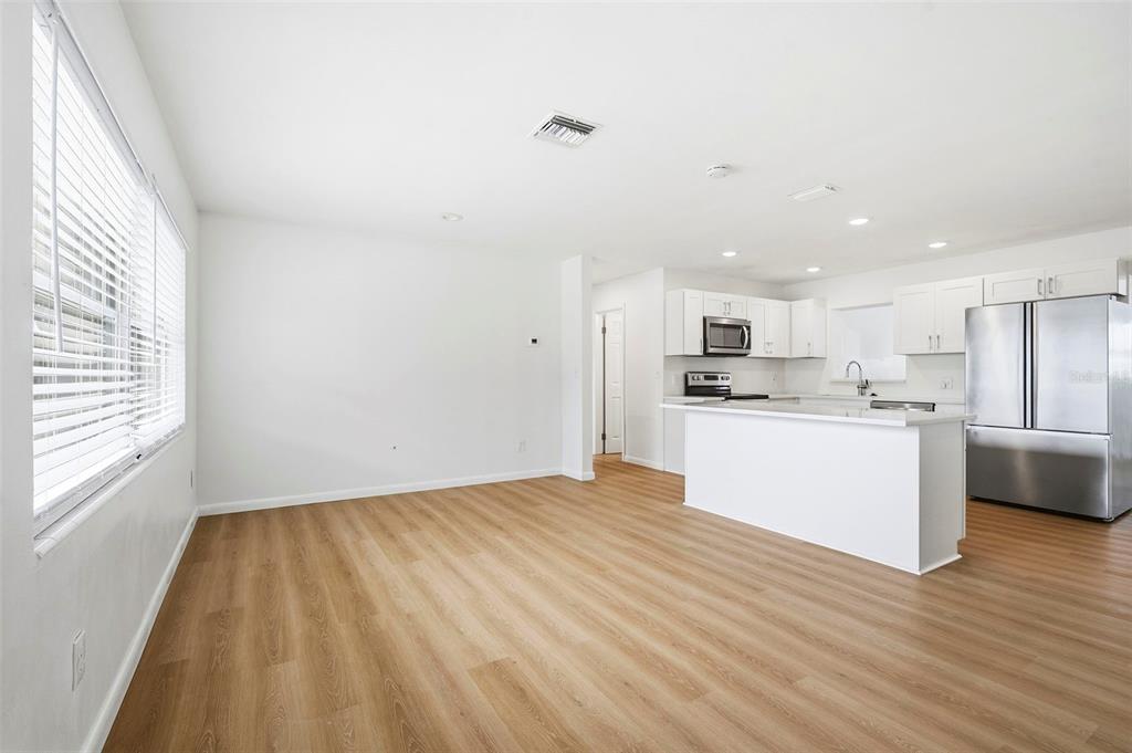 An open-concept kitchen and living area features white cabinetry, stainless steel appliances, and wood flooring — 11354 123RD TERRACE N, LARGO, FL