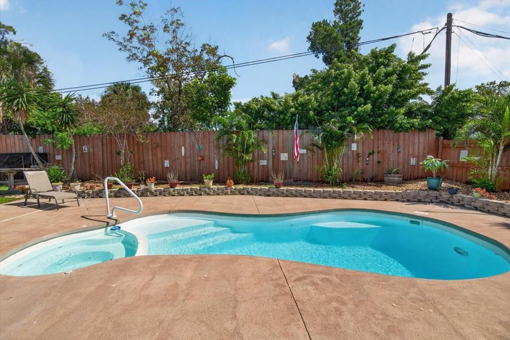 A backyard swimming pool with a spa and a wooden fence under a blue sky — 6205 FAIRWAY BOULEVARD, APOLLO BEACH, FL