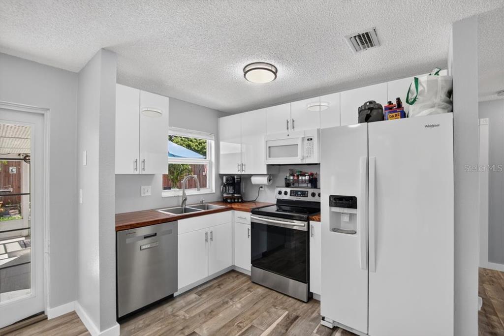 A kitchen with white cabinets, wood countertops, stainless steel appliances, and wood-look flooring — 6205 FAIRWAY BOULEVARD, APOLLO BEACH, FL
