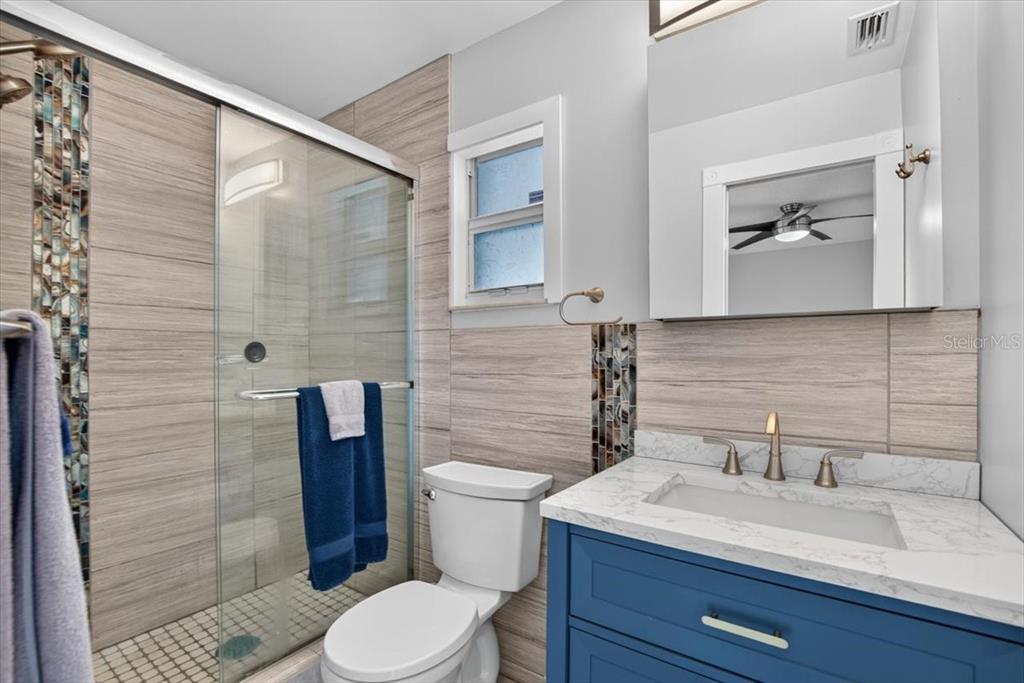 A bathroom features a blue vanity with a marble countertop, a toilet, and a tiled shower — 6205 FAIRWAY BOULEVARD, APOLLO BEACH, FL