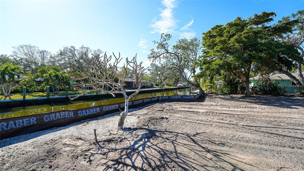 A vacant, cleared waterfront lot features a silt fence and mature trees under a blue sky — 660 LONGVIEW DRIVE, LONGBOAT KEY, FL