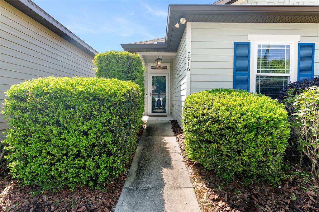 A concrete walkway leads to the front entrance of a house with light-colored siding — 7916 SW 80TH DRIVE, GAINESVILLE, FL
