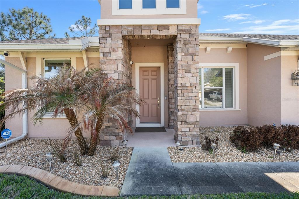The exterior of a house features a stone-accented entryway, a light-colored door, and landscaping — 685 ALDENHAM LANE, ORMOND BEACH, FL