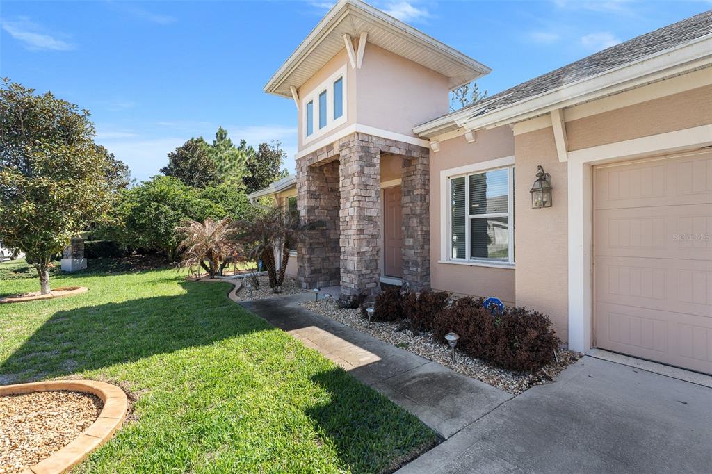 A tan house exterior features a stone-accented entryway, a garage, and a landscaped front yard — 685 ALDENHAM LANE, ORMOND BEACH, FL