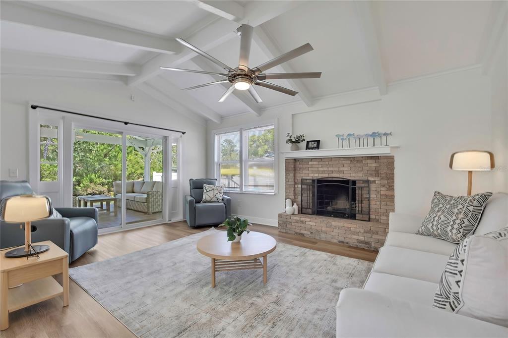 A living room features a brick fireplace, vaulted ceiling, ceiling fan, and sliding glass doors — 6080 WAVERLY ROAD, WEEKI WACHEE, FL