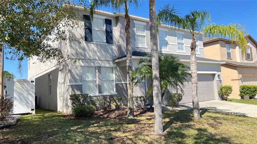 A two-story suburban house with a tan stucco exterior, dark shutters, and palm trees — 1113 PINE RIDGE DRIVE, DAVENPORT, FL