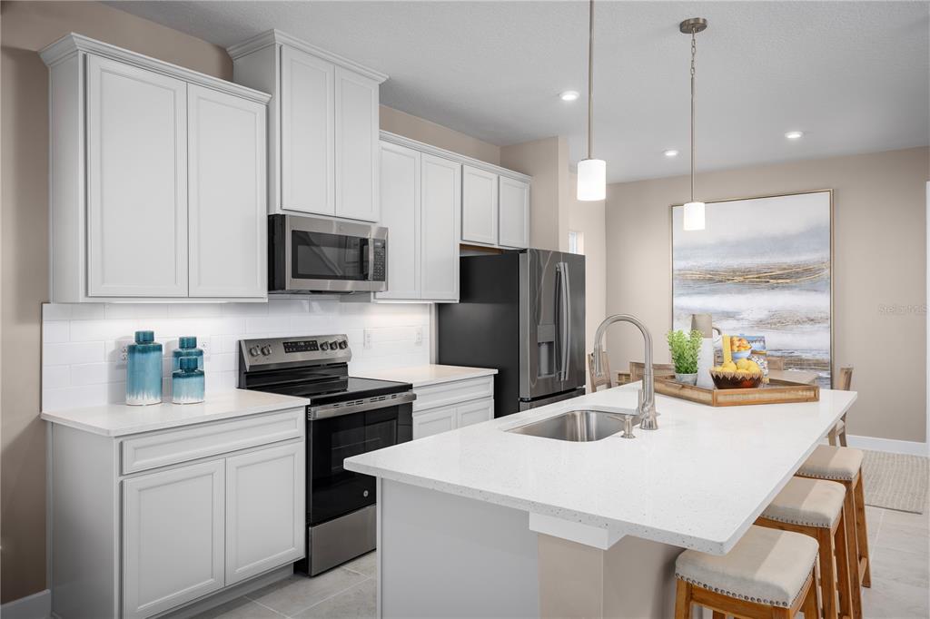 A modern kitchen features white cabinets, stainless steel appliances, a quartz island, and pendant lighting — 663 STONELEIGH LANE, DEBARY, FL