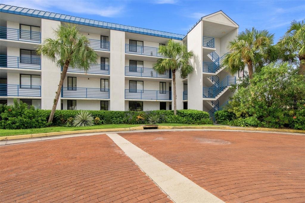 A multi-story apartment building with blue railings and palm trees sits behind a brick driveway — 2424 W TAMPA BAY BOULEVARD UNIT L404, TAMPA, FL