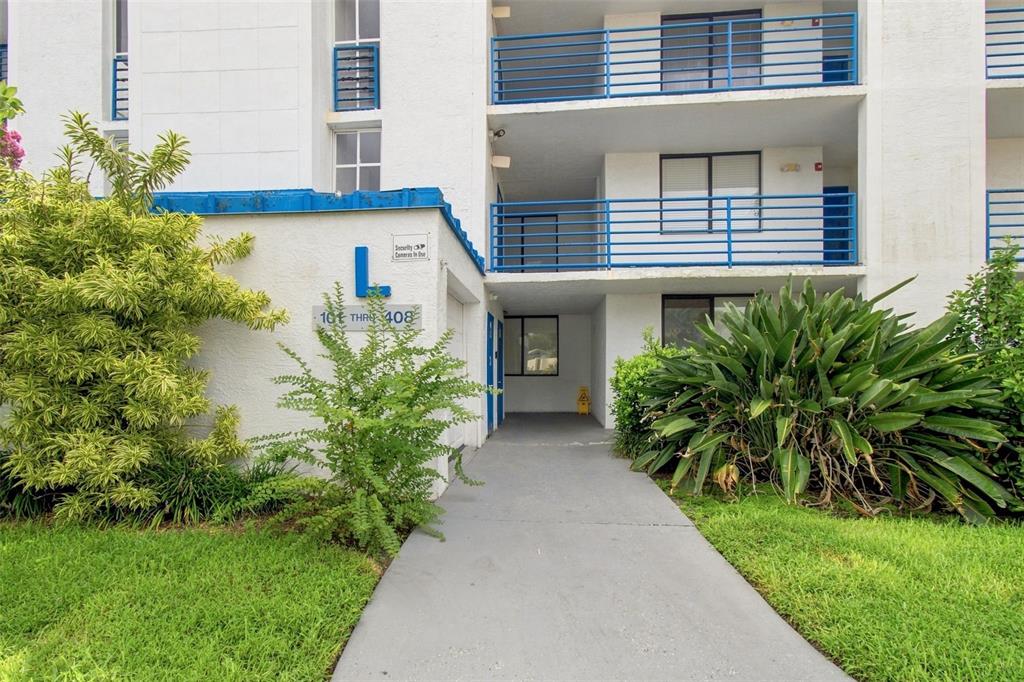 A concrete walkway leads to the entrance of a white apartment building labeled L — 2424 W TAMPA BAY BOULEVARD UNIT L404, TAMPA, FL