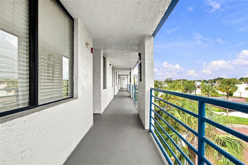 An outdoor apartment walkway features a gray concrete floor, white walls, and blue metal railings — 2424 W TAMPA BAY BOULEVARD UNIT L404, TAMPA, FL