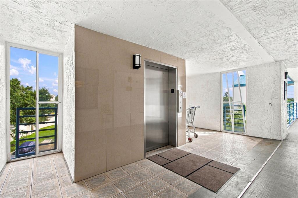 An elevator stands in a tiled hallway with white textured walls and two glass doors — 2424 W TAMPA BAY BOULEVARD UNIT L404, TAMPA, FL