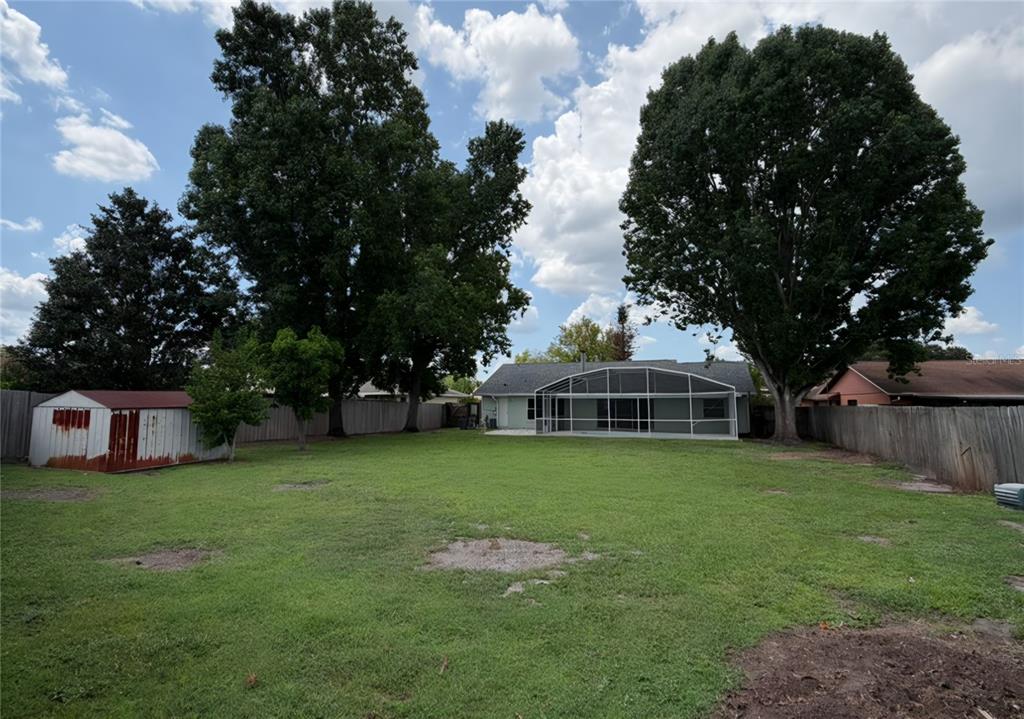 A large backyard features a house with a screened-in patio, two large trees, and a shed — 2658 CERAM AVENUE, ORLANDO, FL