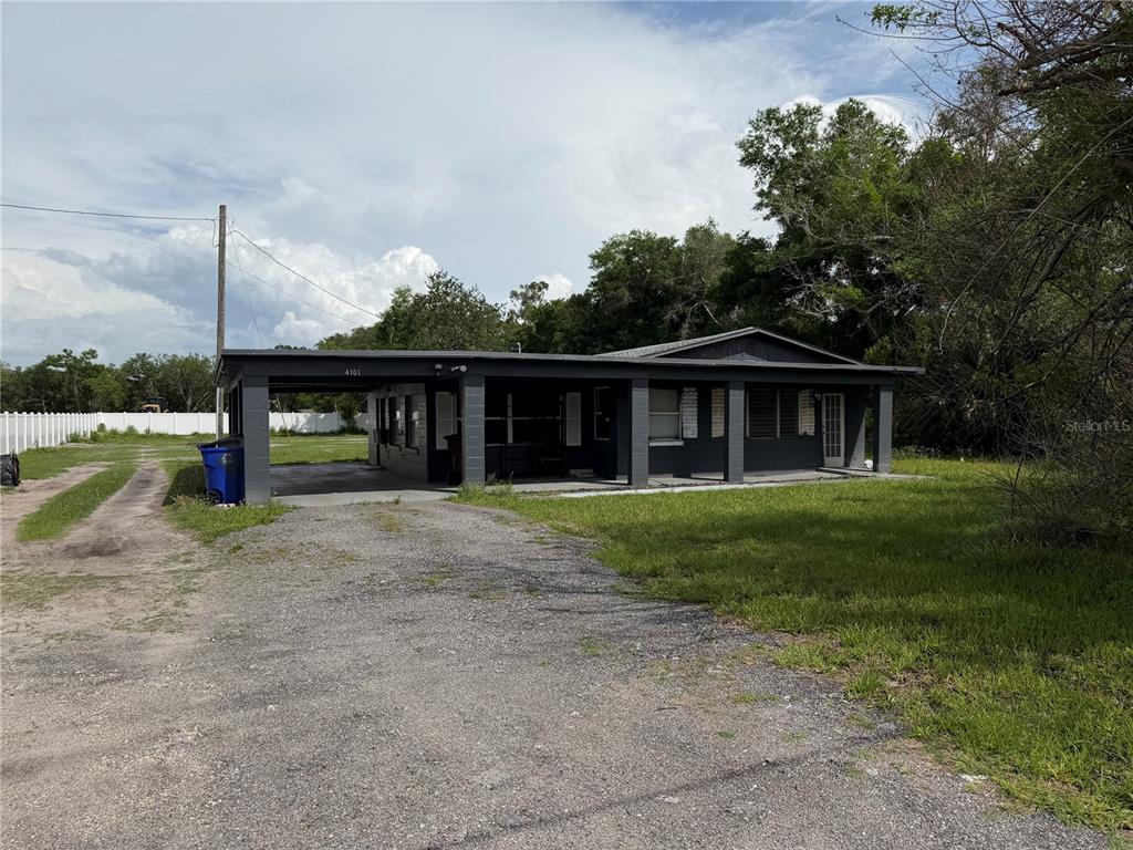 A single-story house with a dark exterior, a large attached carport, and a gravel driveway — 4075 OLD CANOE CREEK ROAD, ST CLOUD, FL