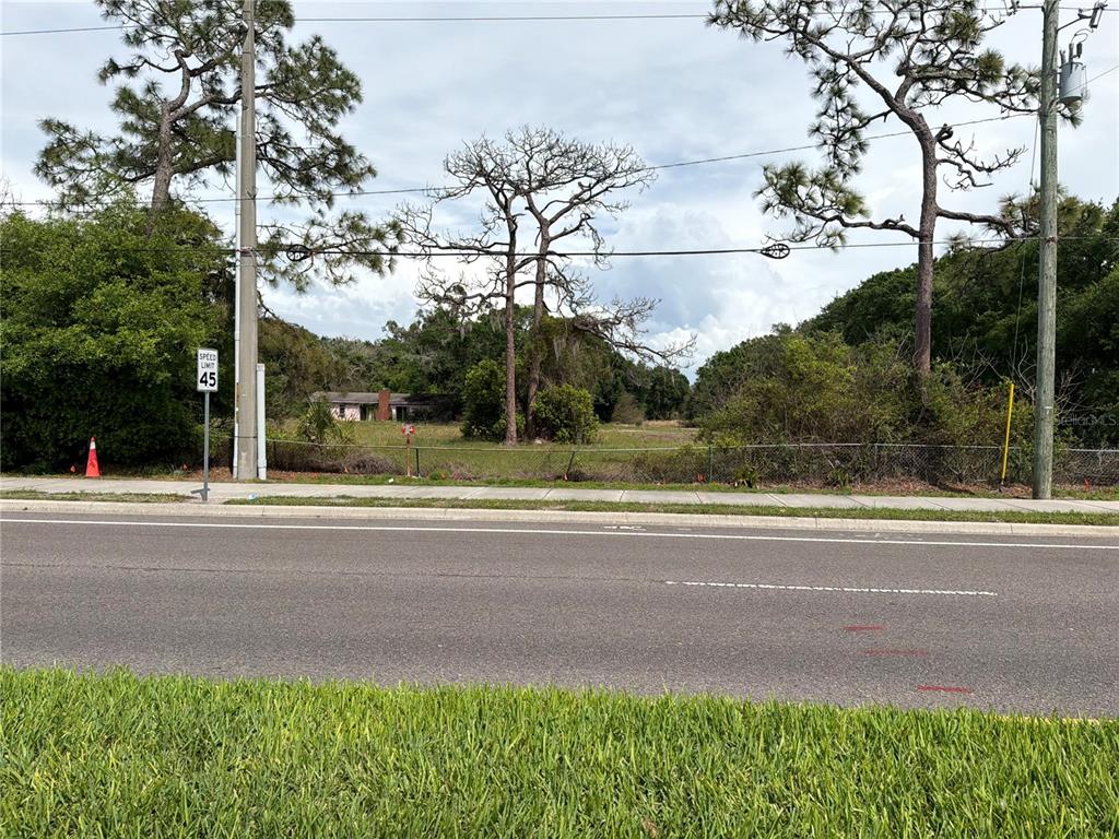 A vacant, grassy lot sits behind a chain-link fence along a paved road — 4075 OLD CANOE CREEK ROAD, ST CLOUD, FL