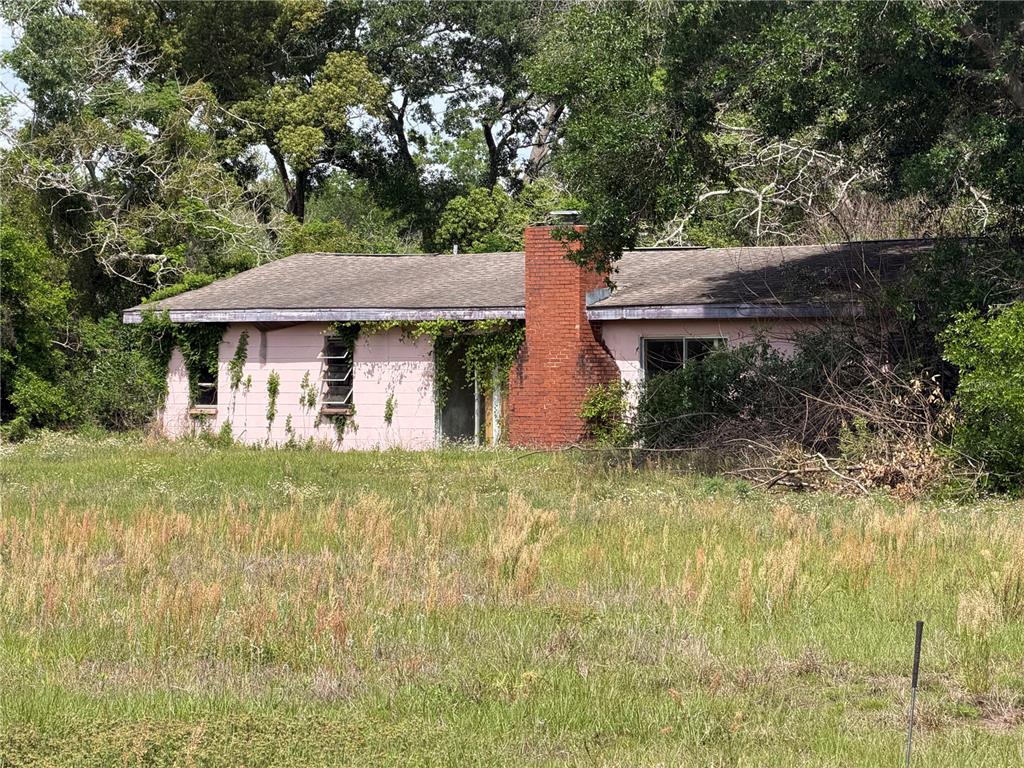 A single-story pink house with a brick chimney sits in an overgrown grassy field — 4075 OLD CANOE CREEK ROAD, ST CLOUD, FL