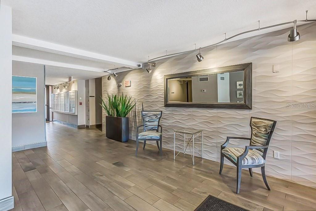 A modern lobby features a textured accent wall, a large mirror, and two patterned chairs — 51 ISLAND WAY UNIT 311, CLEARWATER BEACH, FL