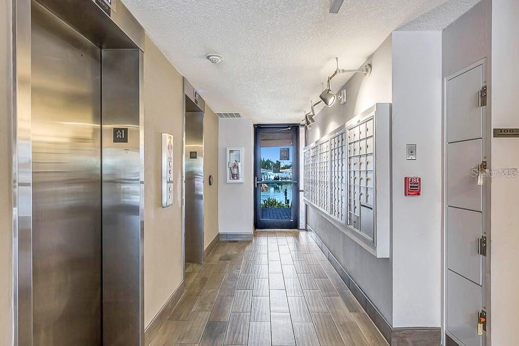 A hallway features two elevators, a wall of mailboxes, and a glass door leading outside — 51 ISLAND WAY UNIT 311, CLEARWATER BEACH, FL