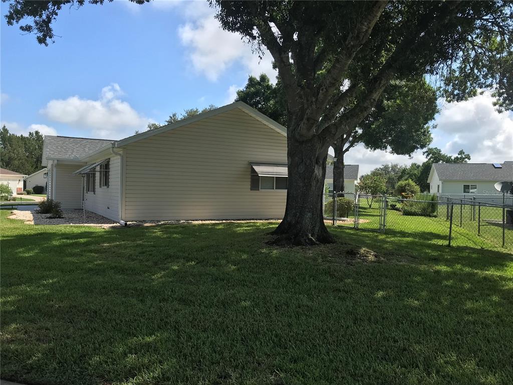 The side view of a light-colored house features a large tree and a chain-link fence — 11879 SW 137TH LOOP, DUNNELLON, FL