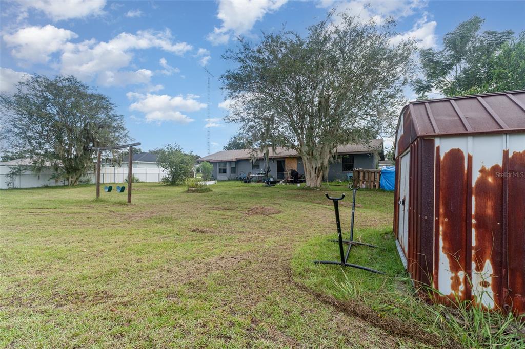 A backyard view featuring a metal shed, a swing set, and a single-story house — 13678 SE 51ST AVENUE, SUMMERFIELD, FL