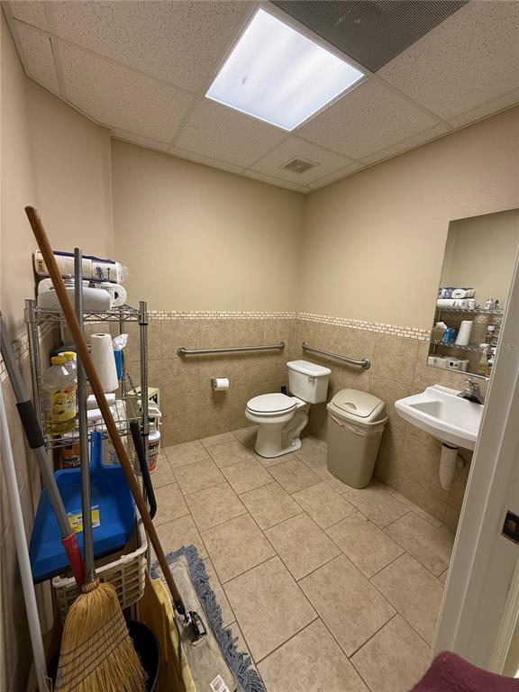A tiled restroom features a toilet, a wall-mounted sink, and a metal storage rack — 107 E 13TH STREET, ST CLOUD, FL