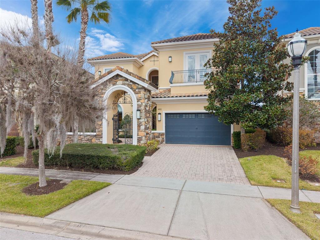 A two-story stucco house with a stone-accented entryway, a balcony, and a paved driveway — 490 MUIRFIELD LOOP, REUNION, FL