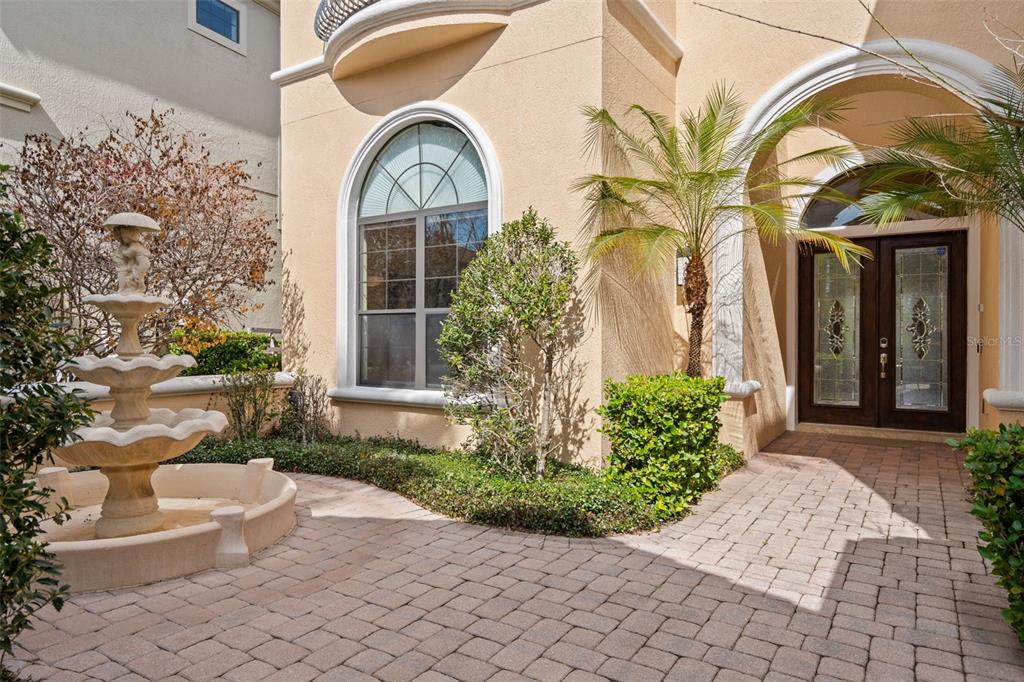 A stone-paved courtyard features a tiered fountain, a palm tree, and a double-door entryway — 490 MUIRFIELD LOOP, REUNION, FL