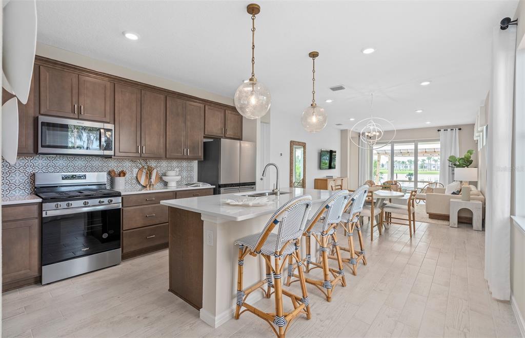 A kitchen with brown cabinets, a white island, and bar stools opens to a dining area — 1167 CROWNING RIDGE WAY, MINNEOLA, FL