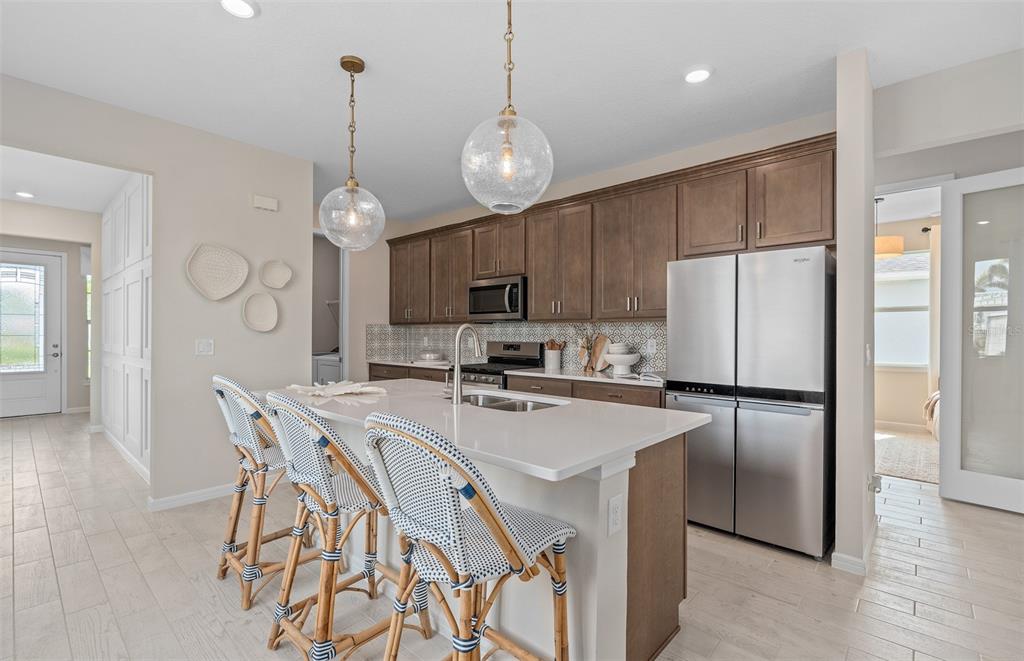 A kitchen features a white island with three stools, stainless steel appliances, and wood cabinetry — 1167 CROWNING RIDGE WAY, MINNEOLA, FL