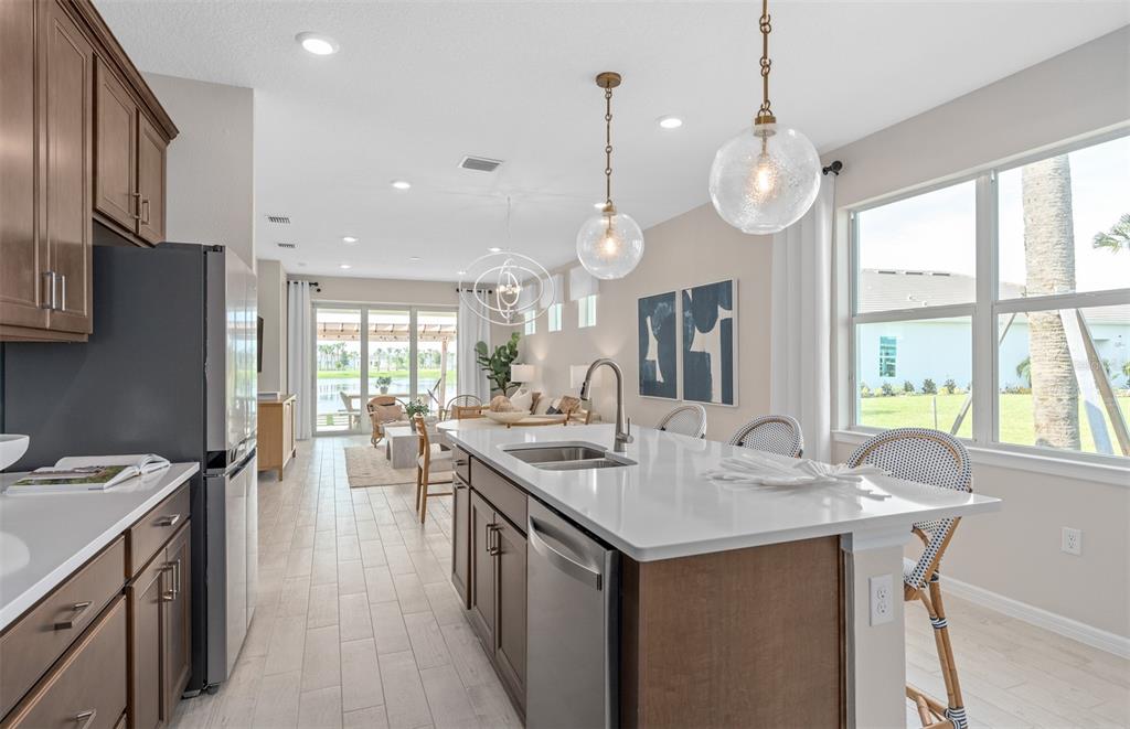 A kitchen with a white island, stainless steel appliances, and wood cabinets overlooks a living area — 1167 CROWNING RIDGE WAY, MINNEOLA, FL