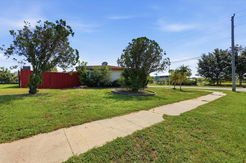 A grassy yard features a sidewalk, two trees, and a red fence beside a house — 4751 S BISCAYNE DRIVE, NORTH PORT, FL