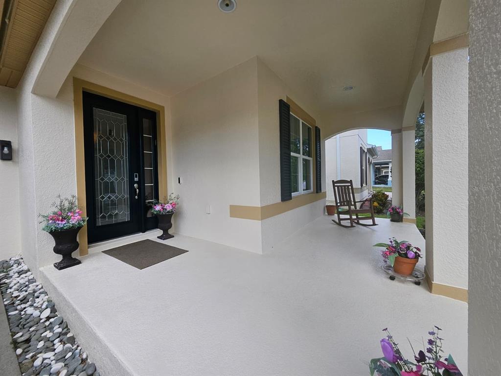 A covered front porch features a black front door, a rocking chair, and potted flowers — 5620 MANGROVE COVE AVENUE, WINTER GARDEN, FL