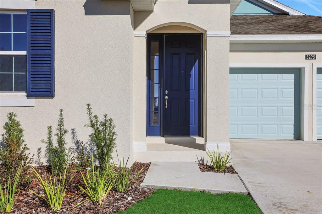 The exterior of a house features a blue front door, a garage, and landscaping — 5295 SPADERDOCK LANE, APOPKA, FL