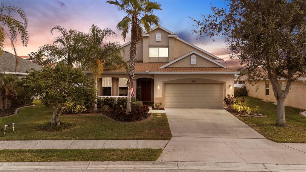 A two-story suburban house with a tan stucco exterior, a two-car garage, and palm trees — 5220 119TH TERRACE E, PARRISH, FL