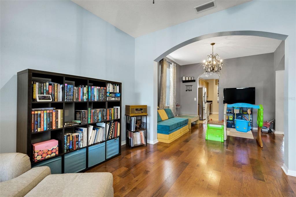 A living room with a large bookshelf, hardwood floors, and an arched entryway to another room — 5220 119TH TERRACE E, PARRISH, FL