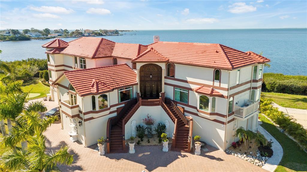 A large, multi-story waterfront home features a prominent double staircase leading to an arched entryway — 2115 ALEXIS COURT, TARPON SPRINGS, FL