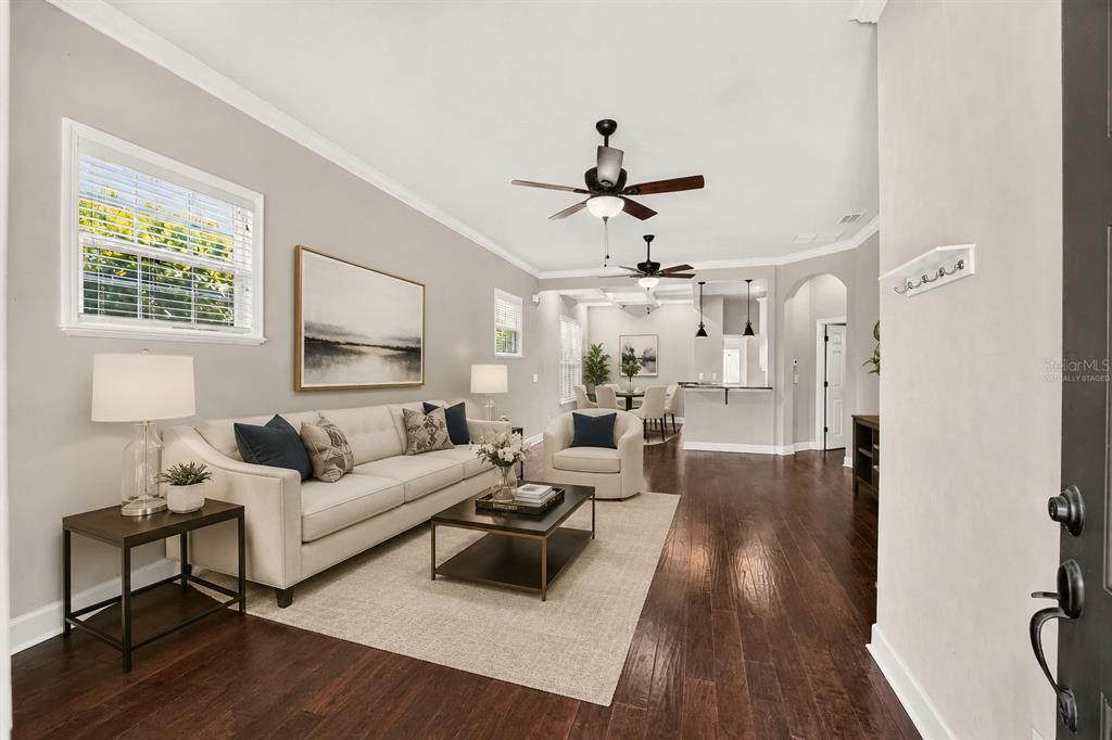 A living room with hardwood floors, a beige sofa, and a dining area in back — 7689 SW 24TH LANE, GAINESVILLE, FL