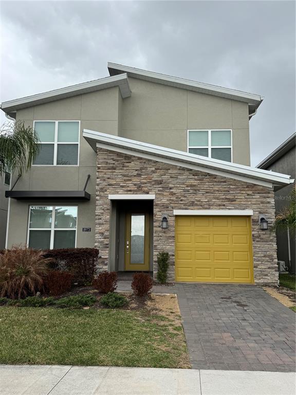 A two-story house with a stone facade, a yellow garage door, and a paved driveway — 8973 PLAY THROUGH DRIVE, DAVENPORT, FL