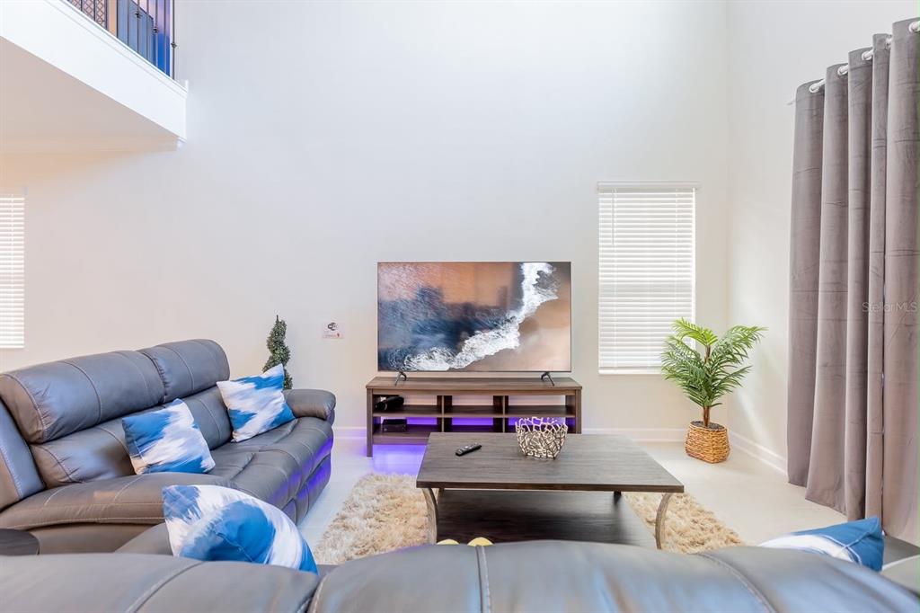 A living room features a gray leather sofa, a television on a stand, and high ceilings — 8973 PLAY THROUGH DRIVE, DAVENPORT, FL