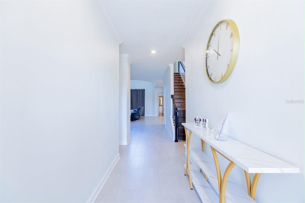 A bright hallway features a white console table, a large wall clock, and a staircase — 8973 PLAY THROUGH DRIVE, DAVENPORT, FL