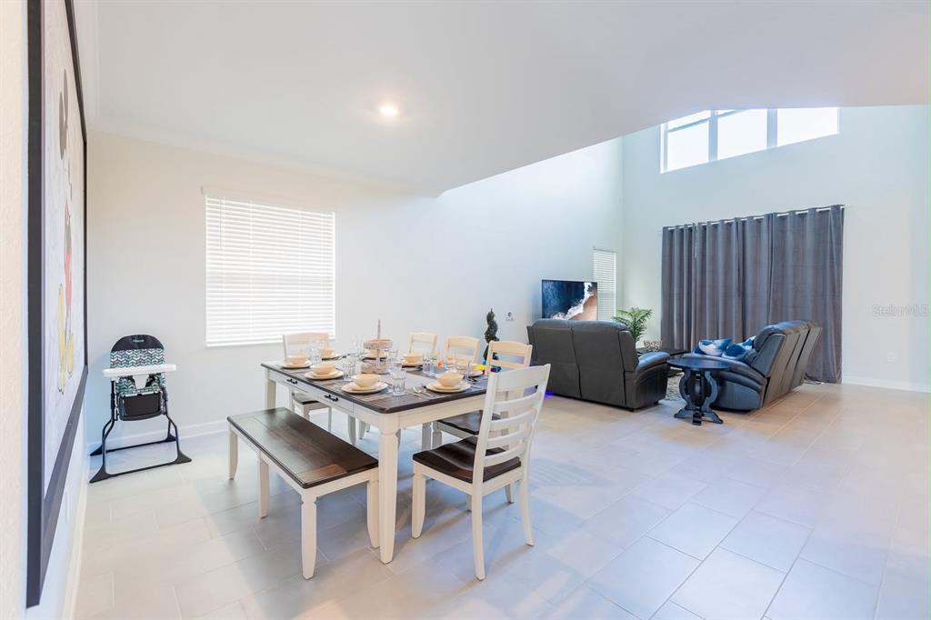 An open-concept dining and living area features tile flooring, a dining set, and vaulted ceilings — 8973 PLAY THROUGH DRIVE, DAVENPORT, FL