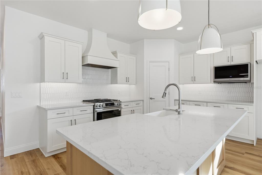 A modern kitchen features white cabinetry, a large quartz island, and stainless steel appliances — 1064 SW 67TH WAY, GAINESVILLE, FL