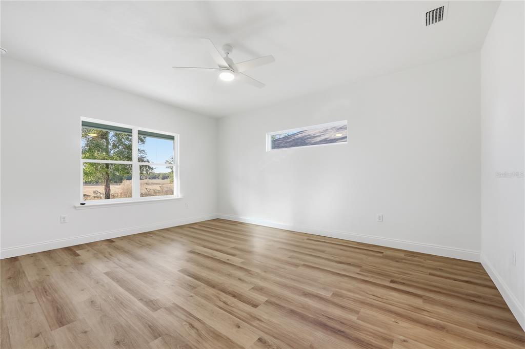 An empty bedroom features white walls, wood-look flooring, a ceiling fan, and two windows — 1064 SW 67TH WAY, GAINESVILLE, FL