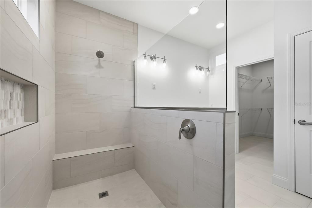 A modern walk-in shower features light gray tile walls, a built-in bench, and glass partitions — 1064 SW 67TH WAY, GAINESVILLE, FL